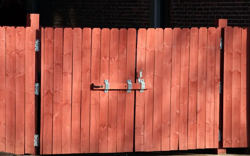 Red-painted wooden privacy fence and gate with a metal latch