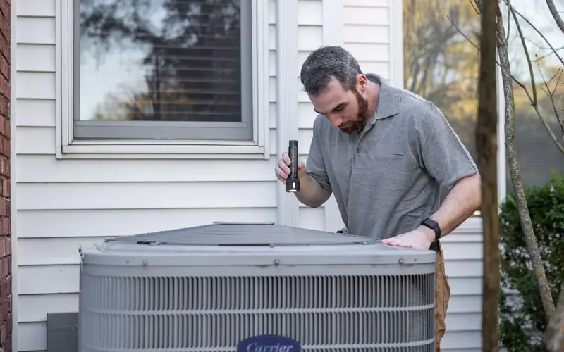 Technician servicing an outdoor air conditioner condenser beside a house
