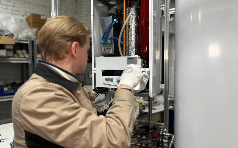 Technician working on water-heating equipment beside a large white hot-water storage tank